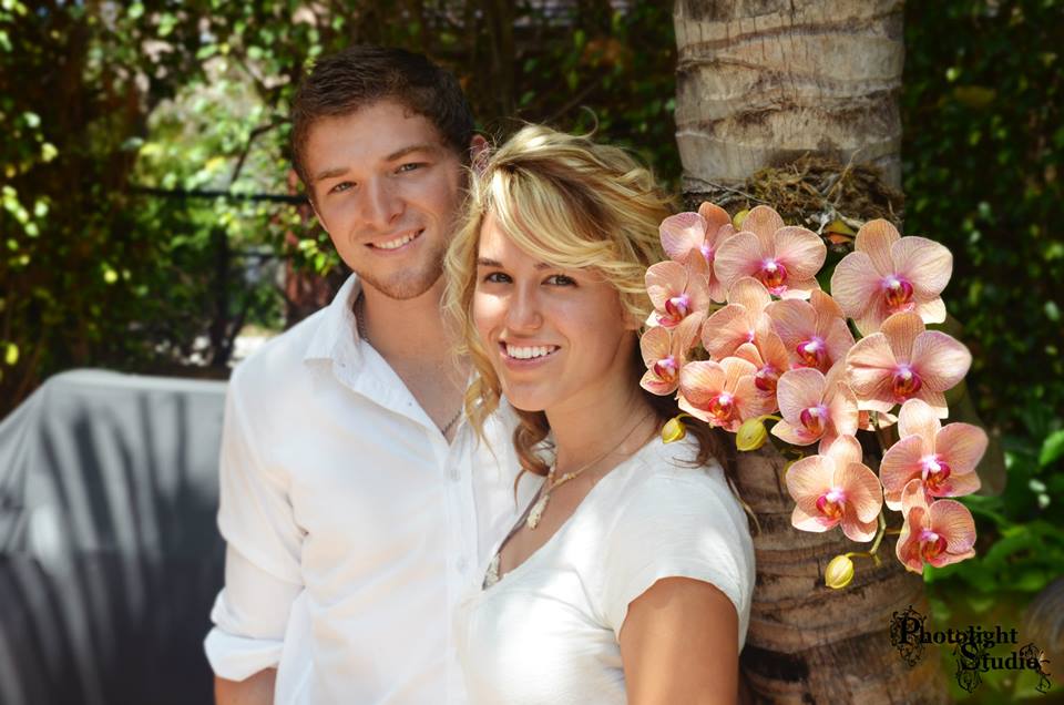 Two women smiling outdoors with a bouquet of pink orchids.