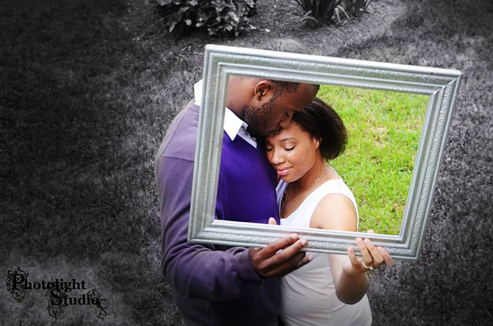 A couple sharing a tender moment framed by a picture frame outdoors.