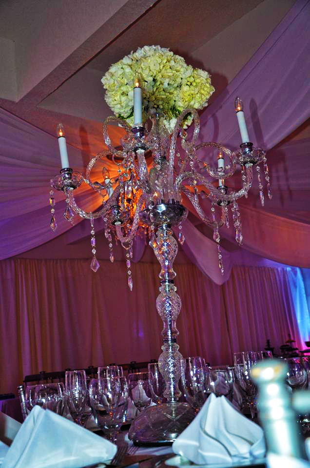Elegant crystal chandelier with candles hanging from a purple draped ceiling.
