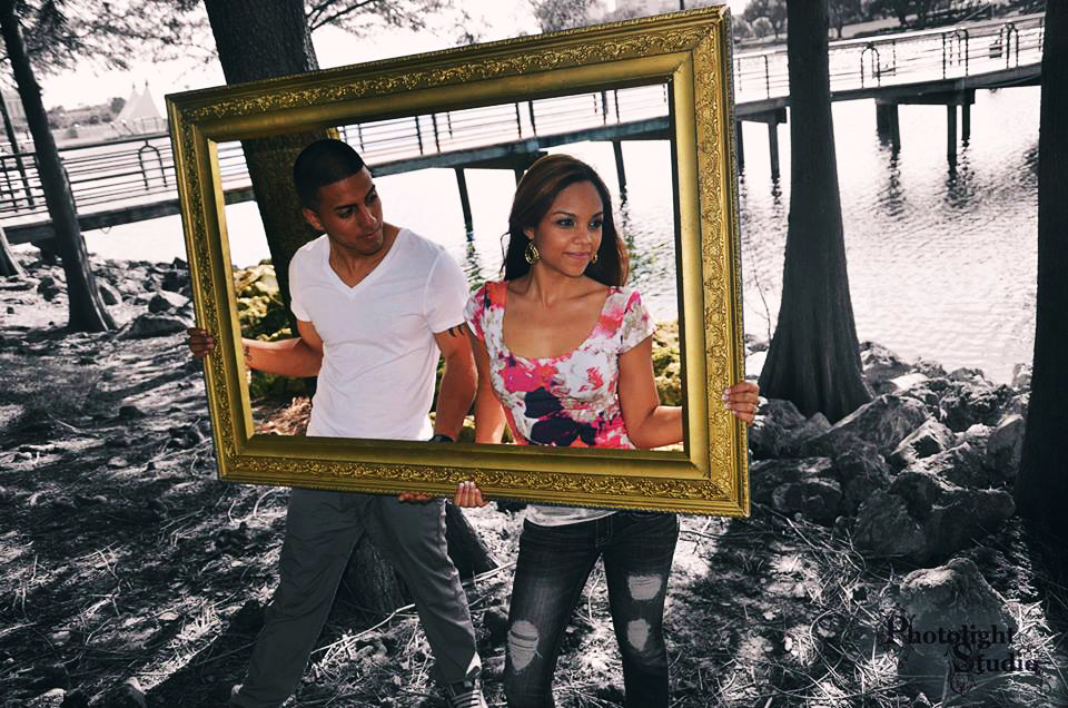 Two people holding a large empty picture frame outdoors.