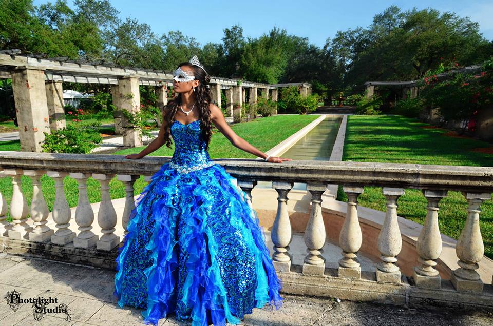 Young woman in an elegant blue ball gown poses in a lush garden.