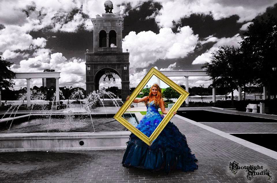 A woman in a blue gown framed by a golden picture frame in front of a historic bell tower.