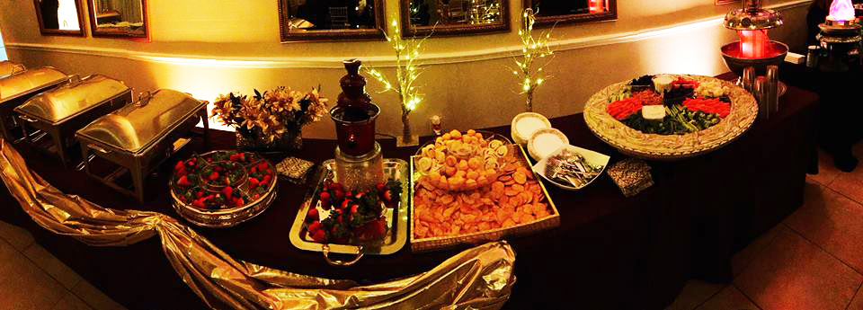 A festive table with a chocolate fountain and assorted snacks under warm lights.