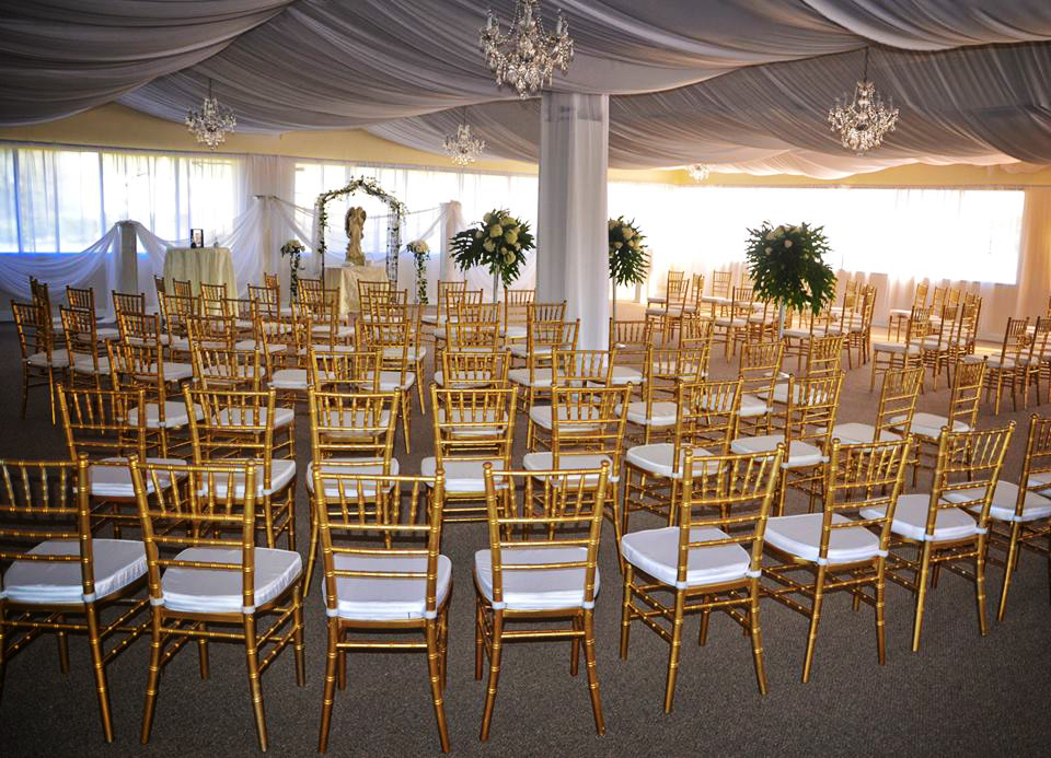 Elegant gold chairs arranged for a formal event in a decorated tent.