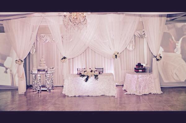 Elegant wedding reception setup with white drapes and floral centerpiece.