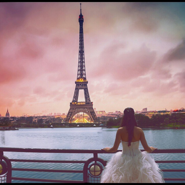 Bride in wedding dress gazes at Eiffel Tower at sunset.