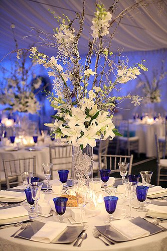 Elegant floral centerpiece with white blossoms on a banquet table with blue glassware.
