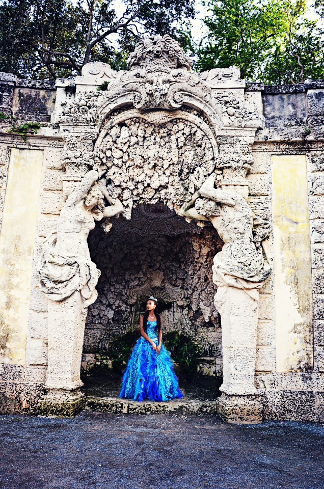 Woman in a vibrant blue dress stands in an ornate stone archway.