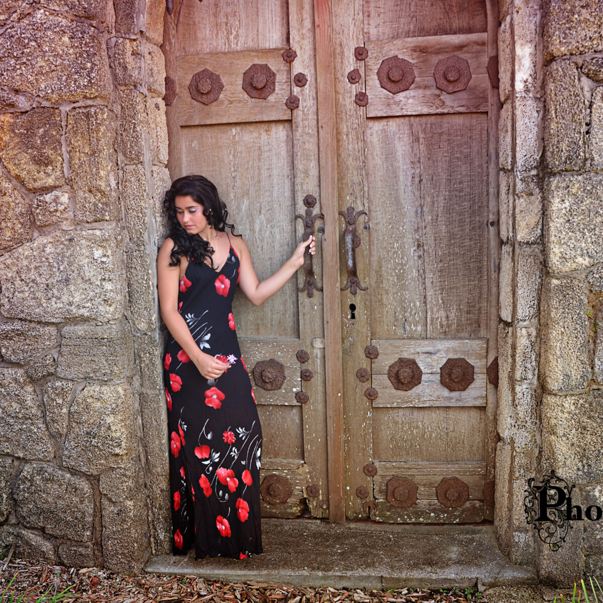 Woman in a floral dress poses by an ancient wooden door.