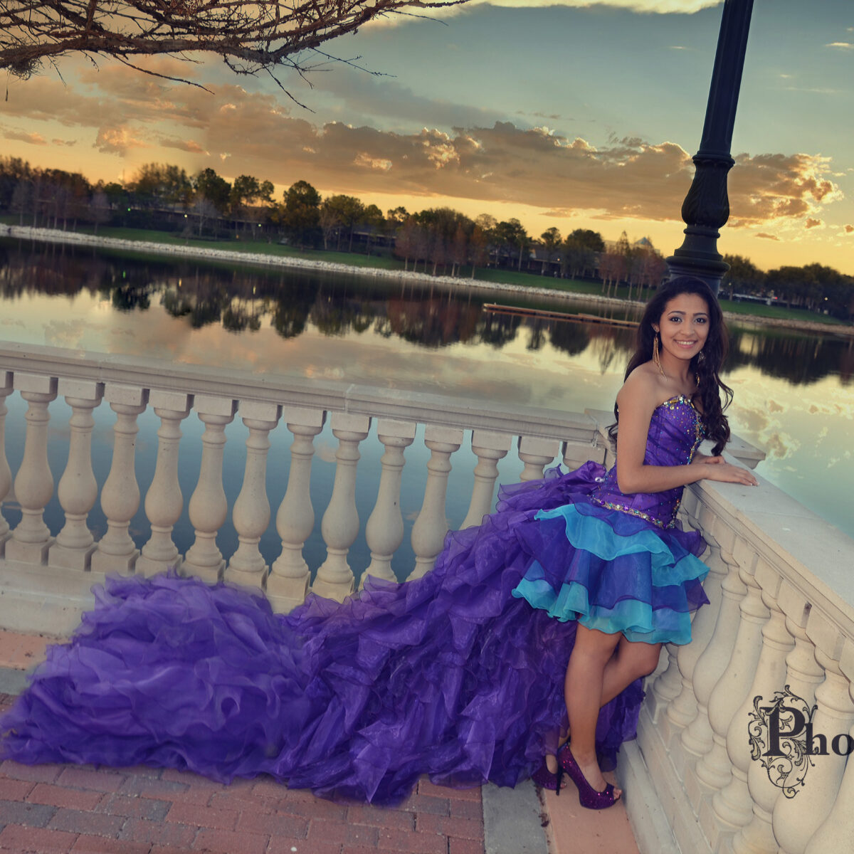 Young woman in a vibrant purple and blue dress by a lakeside at sunset.