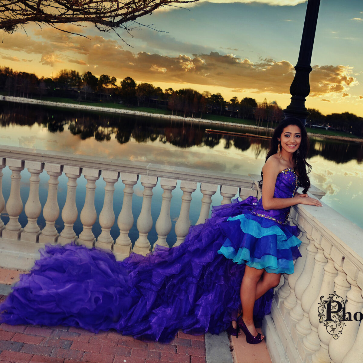 Young woman in a vibrant purple and blue dress by a lakeside at sunset.