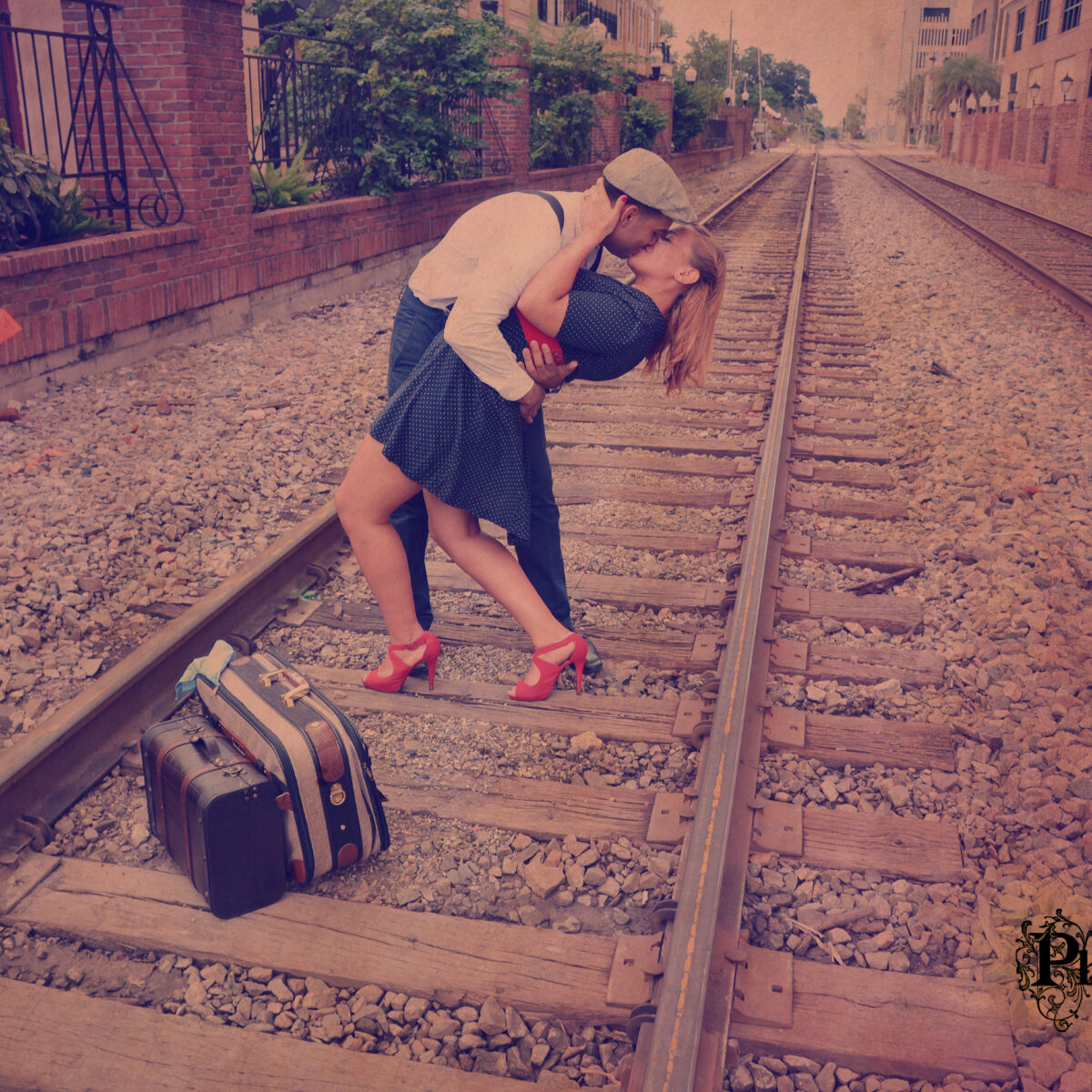 Couple passionately kissing on railway tracks with vintage suitcases beside them.