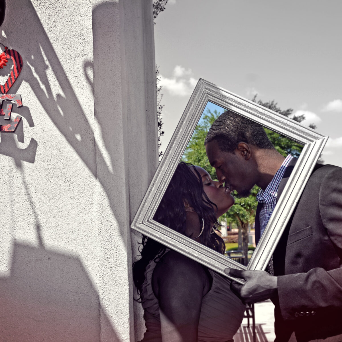 A couple shares a kiss reflected in a handheld mirror outdoors.
