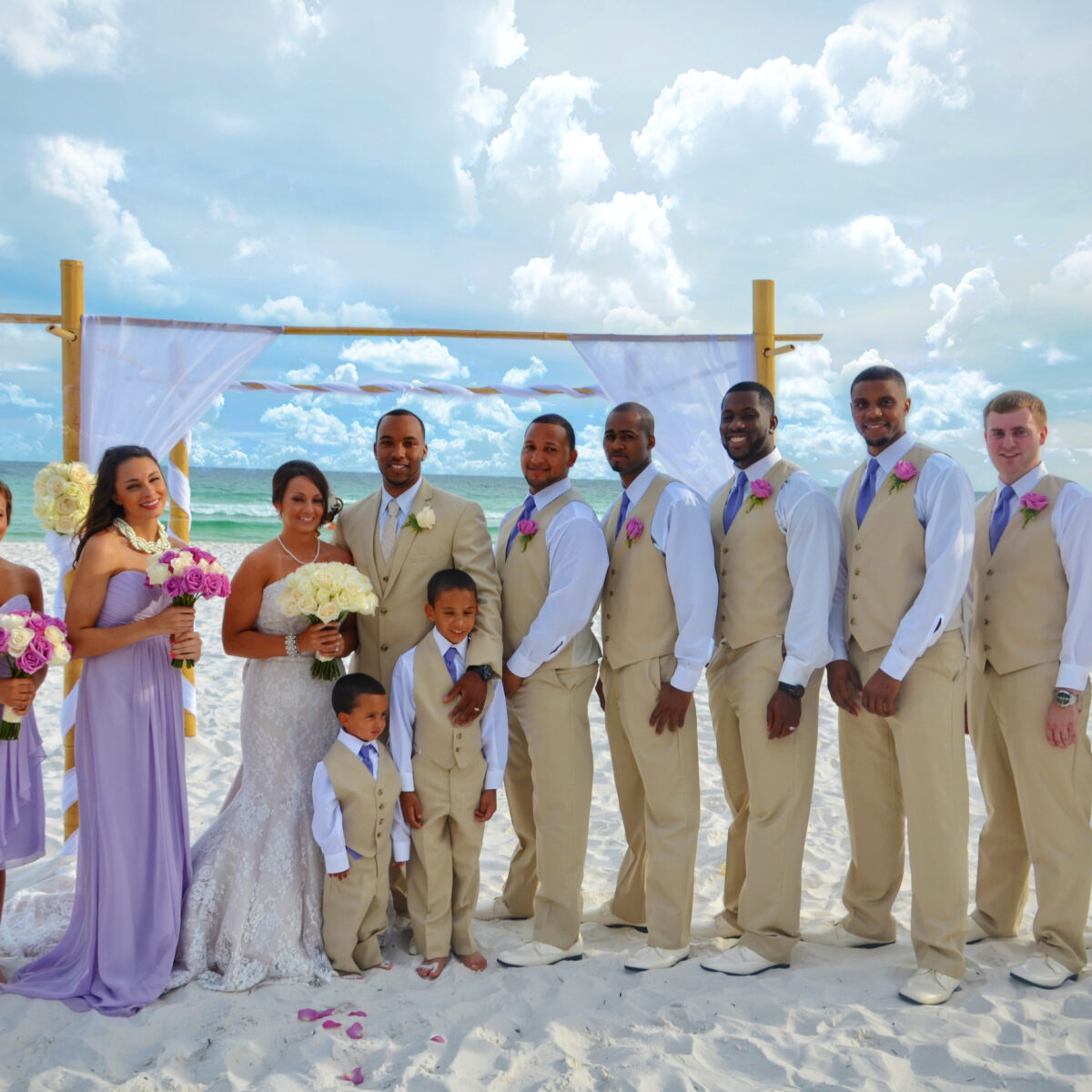 A wedding party posing on a sunny beach with blue skies and white sand.
