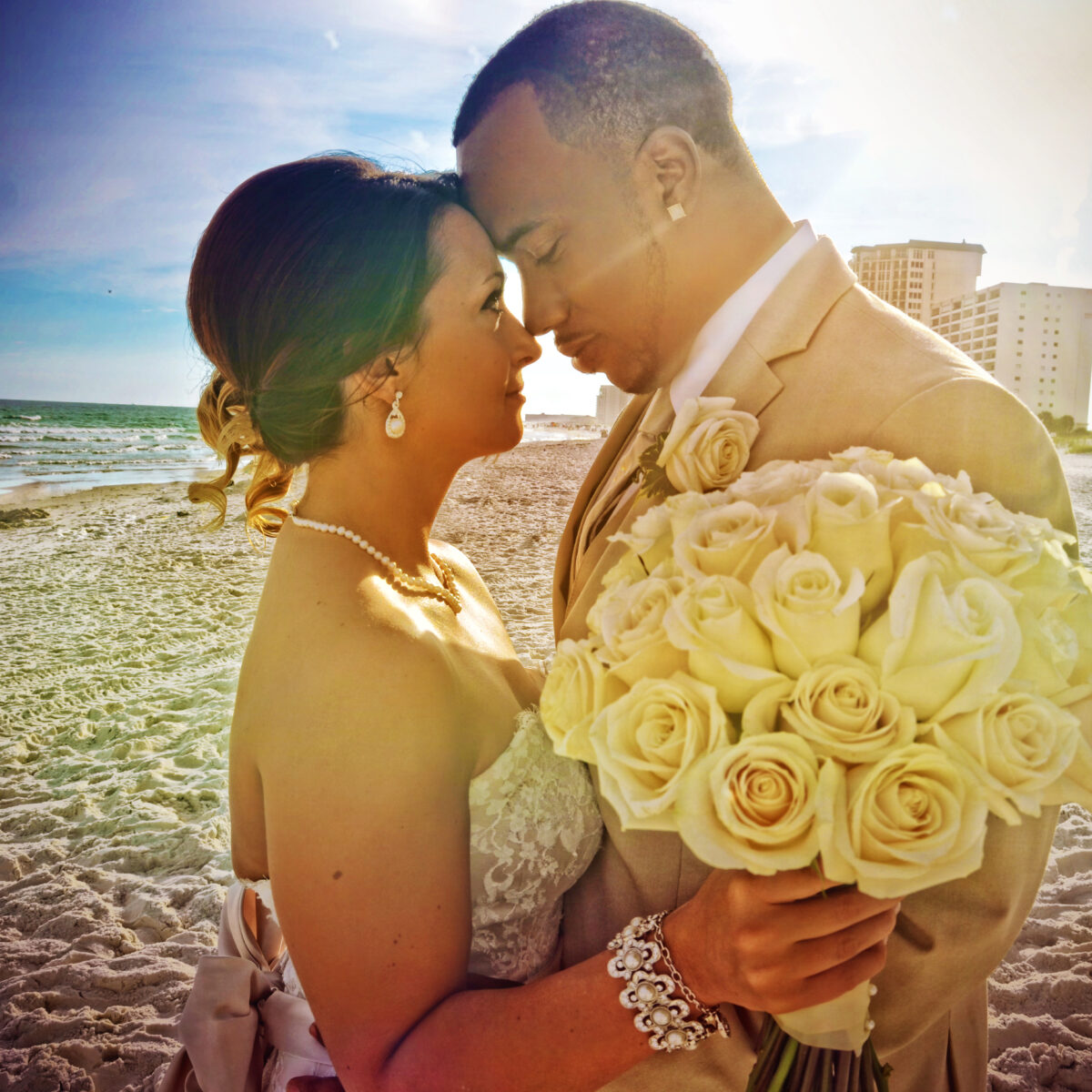 Bride and groom share a tender moment on a beach at sunset.