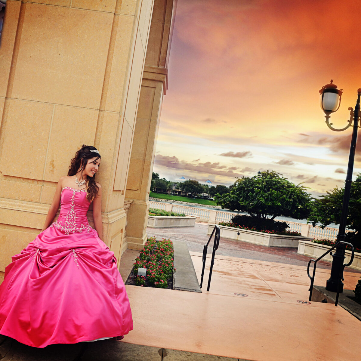 Woman in elegant pink gown posing by historic architecture at sunset.